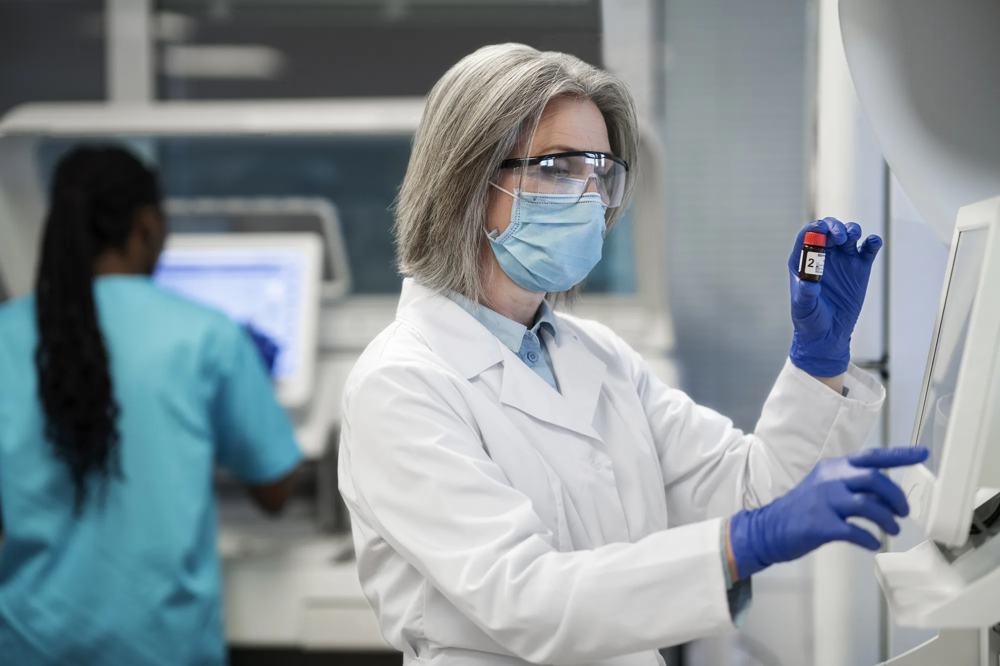 Scientist in a lab coat and gloves inspecting an amber glass vial